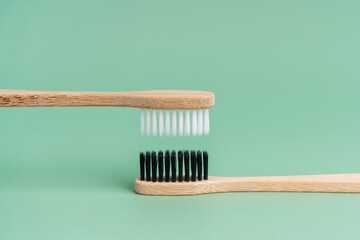 Two Eco-friendly antibacterial bamboo wood toothbrushes with white and black bristles on a light green background. Taking care of the environment is trending. Tolerance. Copy space