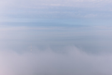 Obraz na płótnie Canvas Silhouette of high television or electric tower seen slighty among thick clouds of morning fog and mist. Unusual morning panorama of dramatic landscape.
