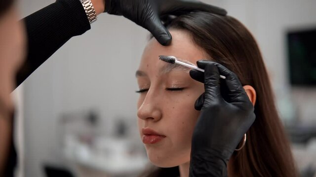 The master cleans the eyebrows of a young girl with an eyebrow foam.Eyebrow correction