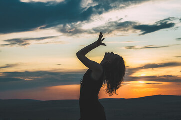 Silhouette of a a young woman dancing in the sunset on a hill. Concept: freedom, outdoor...