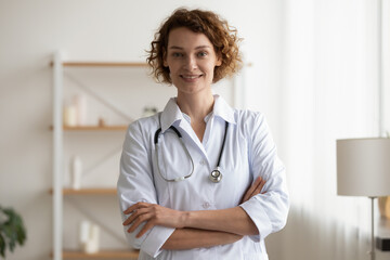 Portrait of smiling young doctor physician in white coat and stethoscope standing in clinic office...