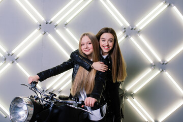 Two beautiful girls wearing costumes of racers and sitting on a motorcycle, in the studio