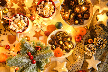 sweet food top view background for merry christmas or new year holiday decoration with night illumination - chocolate candies, tangerines, cookies, marshmallow and cocoa latte on white wood