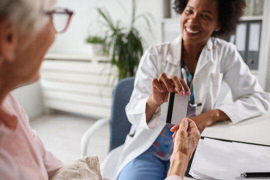 A Female Black Ethnicity Doctor Sits At Her Office And Talking With Elderly Female Patient