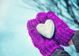 Female hands in knitted mittens with heart of snow in winter day. Love concept. Valentine day background.	