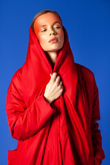 Trendy woman wrapping in red garment against blue background
