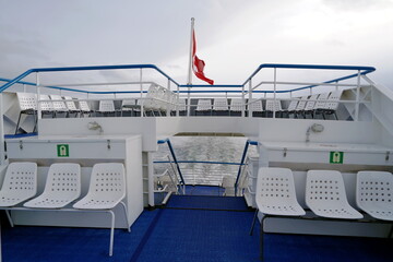 Stem of a tourist ferry on Lake Zurich in Switzerland. White plastic chairs are arranged on three decks and there is Swiss federal flag blowing in wind at the back with dramatic sky on the background.
