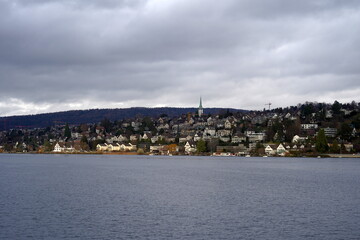 View on the part of the Golden Coast on Lake Zurich in Switzerland with village Zollikon. Photo taken from the lake that is in the foreground and dramatic sky on the background. 