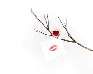White card with lip print hanging on a bare winter tree branch pinned with a clothespin with a red heart for Valentine's Day. On white background isolated