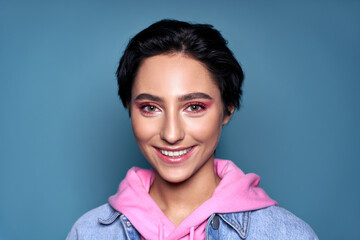 Happy smiling positive stylish cool gen z teen girl, short-haired zoomer teenager with trendy pink makeup on pretty face looking at camera isolated on blue background. Close up headshot portrait. - obrazy, fototapety, plakaty