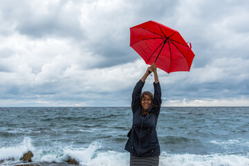Girl with a red umbrella on the background of the sea. Atmospheric autumn landscape with a young...