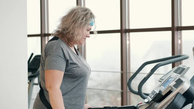 Larger woman exhausted by exercising on treadmill. Weight loss, body positive, sport concept.