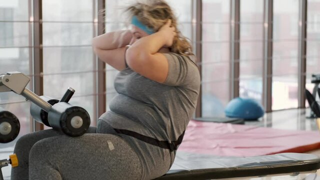 Overweight unhealthy woman doing sit ups at gym, trying to get fit.