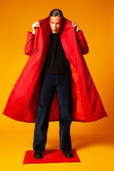 Female model adjusting trendy red coat against yellow background