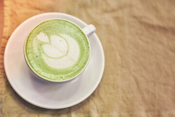 Cup of matcha latte on wooden background and a beige napkin in a cafe with copy space. High quality photo