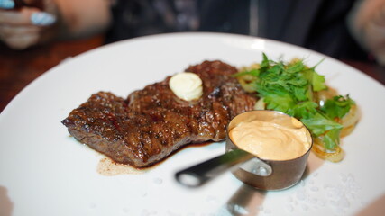 Close up of juicy steak with sauce and vegetables in white plate. Appetizing meat dish with fried onions and greens in restaurant.