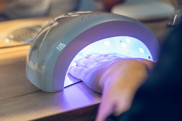 Girl dries her nails covered with gel polish using a UV lamp