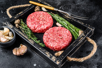 Raw beef meat patties for burger from ground meat and herbs on a wooden board. Black background....