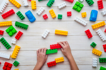 Baby hands playing with colorful plastic blocks on white wooden table background. Developing toys. Learning by playing