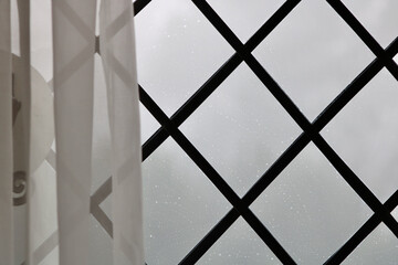 Voile curtain in front of geometric leaded light glass window on rainy day