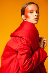 Young woman wrapping in red coat against yellow background