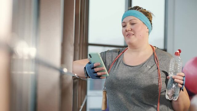 Overweight woman is happy after workout. She is using her phone, talking and doing selfies.