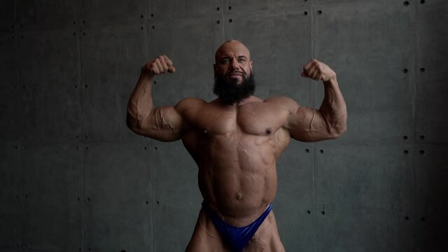 muscleman is demonstrating his muscles at grey background, medium portrait shot