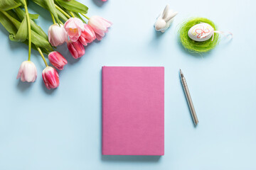 Easter planning with notebook, tulip flowers, egg on blue background. Top view with copy space. Happy Easter greeting card.
