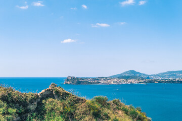 view in the gulf of Naples from Monte di Procida with the islands of Procida and Ischia in the background and vegetation in the foreground, under a blue sky with cloud