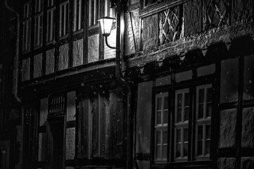 Künstlerische Schwarz-weiß-Aufnahme einer malerischen Gasse mit Fachwerkhäusern bei Schneefall