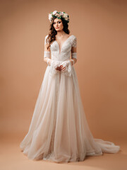 Caucasian young bride in studio on brown background in a white wedding dress and floral garland