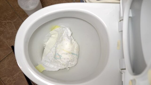 Close-up tossing a dirty baby diaper into the toilet. It clogs the toilet flush