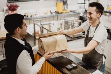 Buys lunch food healthy foods vegetables pasta in a paper bag with a takeaway. small business pizzeria coffee shop. a young male employee picks up dinner. convenient delivery 