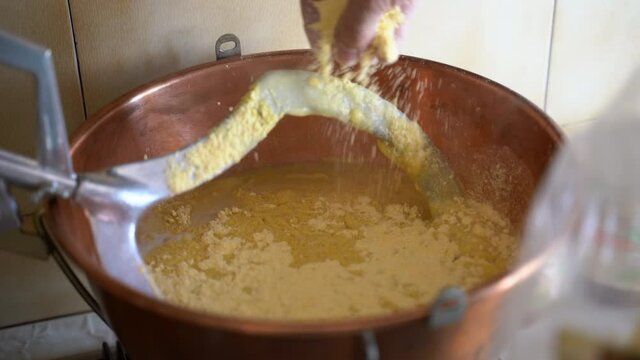 Corn porriage prepared at home, italian winter meal. Pouring and stirring maize flour in cooper pan on low fire, healthy eating and nutrition