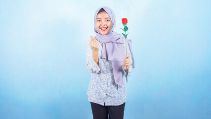 Young Asian Muslim woman holding red rose over blue background