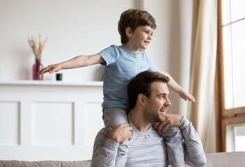 Overjoyed Caucasian dad carry on back engaged in funny game activity with little 6s son on family...