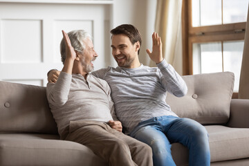 Excited millennial Caucasian man and senior father relax at home give high five make deal. Smiling...