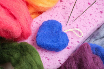 Obraz na płótnie Canvas blue wool heart felting process, needles for felting, sponge and wool on the table, handmade romantic gift