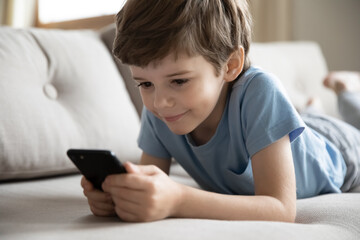 Close up of cute little 7s Caucasian boy child look at cellphone screen play online game on gadget. Happy small preschooler kid have fun using smartphone device with wireless internet connection.