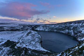 Beautiful evening view over Lough Bray Upper lake and Wicklow Mountains seen from Eagles Crag, Ballylerane, Co. Wicklow, Ireland on a frosty day. Snow in Ireland. Purple cold sunset