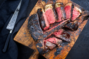 Traditional barbecue dry aged wagyu t-bone beef steak bistecca alla Fiorentina sliced and served with black salt as top view on an old rustic wooden board