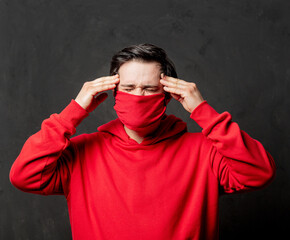 guy in red sweatshirt and face mask with headache on dark background