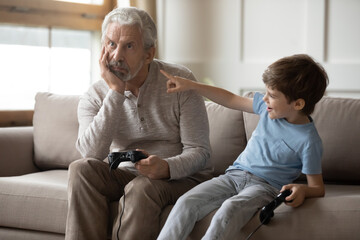 Mature Caucasian grandfather and little preschooler grandson play computer video games together....