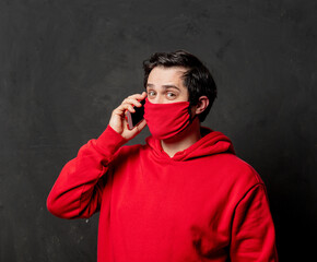 guy in red sweatshirt and face mask using mobile phone on dark background