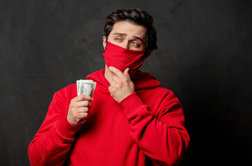 guy in red sweatshirt and face mask hold money in hand on dark background