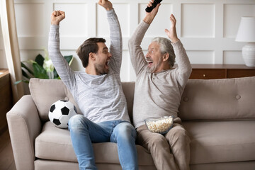 Excited millennial Caucasian man with elderly father feel euphoric celebrate win watch football...