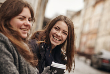 Outdoors fashion portrait of two young beautiful women friends drinking coffee.