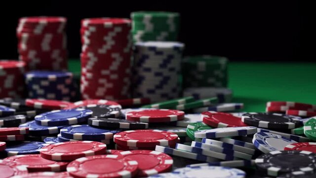 Poker chips at stake are on a green table in close-up. Equipment for playing at hazard games in a casino on black background. Winning and losing money theme. Gambling as entertainment at leisure time.