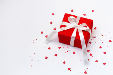 Red gift box with white ribbon bow and small sugar hearts on a white background. Flat lay, top view, overhead. Valentine's Day banner or greeting card.