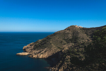 Fototapeta na wymiar Lighthouse on rocky cliffs in deep blue ocean bay in the natural park 'Serra Gelada' in Albir, Spain
